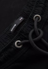 Primer plano de una cintura elástica negra con cordón pasado a través de ojales metálicos etiquetados como "ombre wear."