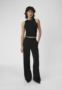 Top corto negro de canalé combinado con pantalones de pierna ancha negros de cintura alta y zapatos negros de punta, creando una silueta estilizada.