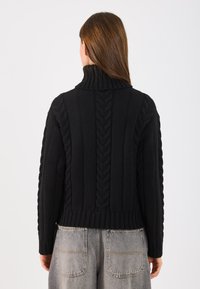 Mustalti kudumis-sviiter kõrge kaelusega, tekstuursete nöörkudumise mustrite, ribakäiste ja lühendatud hemiga.