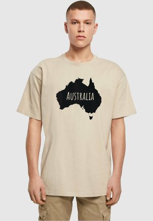 Beige bomulds t-shirt med en stor sort silhuet af Australien og ordet "AUSTRALIEN" trykt i hvidt. Korte ærmer, afslappet pasform.