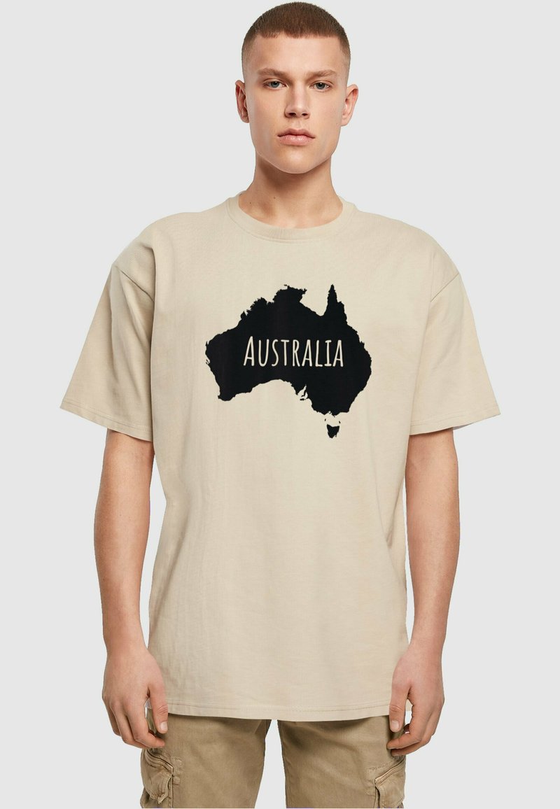 Smėlinės spalvos medvilninė marškinėliai su dideliu juodu Australijos siluetu ir žodžiu "AUSTRALIJA" atspausdintu baltai. Trumpomis rankovėmis, laisvas kirpimas.
