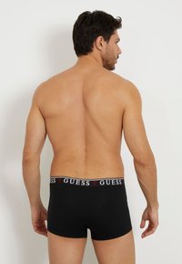Boxeri din bumbac negru, cu un brâu contrastant ce prezintă logo-ul Guess, arătați din spate. Textură netedă și design ajustat.