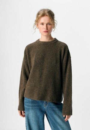 Brauner Strickpullover mit rundem Ausschnitt, langen Ärmeln und einer dezent strukturierten Oberfläche. Kombiniert mit hellblauen Jeans.