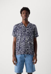 Camisa de manga curta azul-marinho com padrões abstratos brancos, apresentando um colarinho em notch, combinada com calções de ganga azul-claro.
