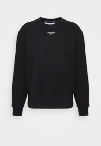 Sudadera de cuello redondo negra de Calvin Klein Jeans con puños y dobladillo acanalados, texto del logo blanco centrado debajo del cuello.
