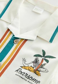Short-sleeve polo shirt in cream with teal, orange, and yellow vertical stripes. Features a palm tree graphic and a button closure at the collar.