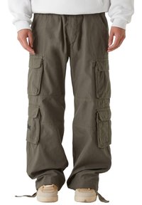 Zielone oliwkowe spodnie cargo wykonane z wytrzymałego materiału, z wieloma dużymi kieszeniami, luźnym krojem i regulowanymi trokami na kostkach.