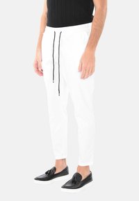 Pantaloni bianchi a sigaretta con vita regolabile e dettagli neri, abbinati a scarpe nere senza lacci con un elegante fiocco decorativo.
