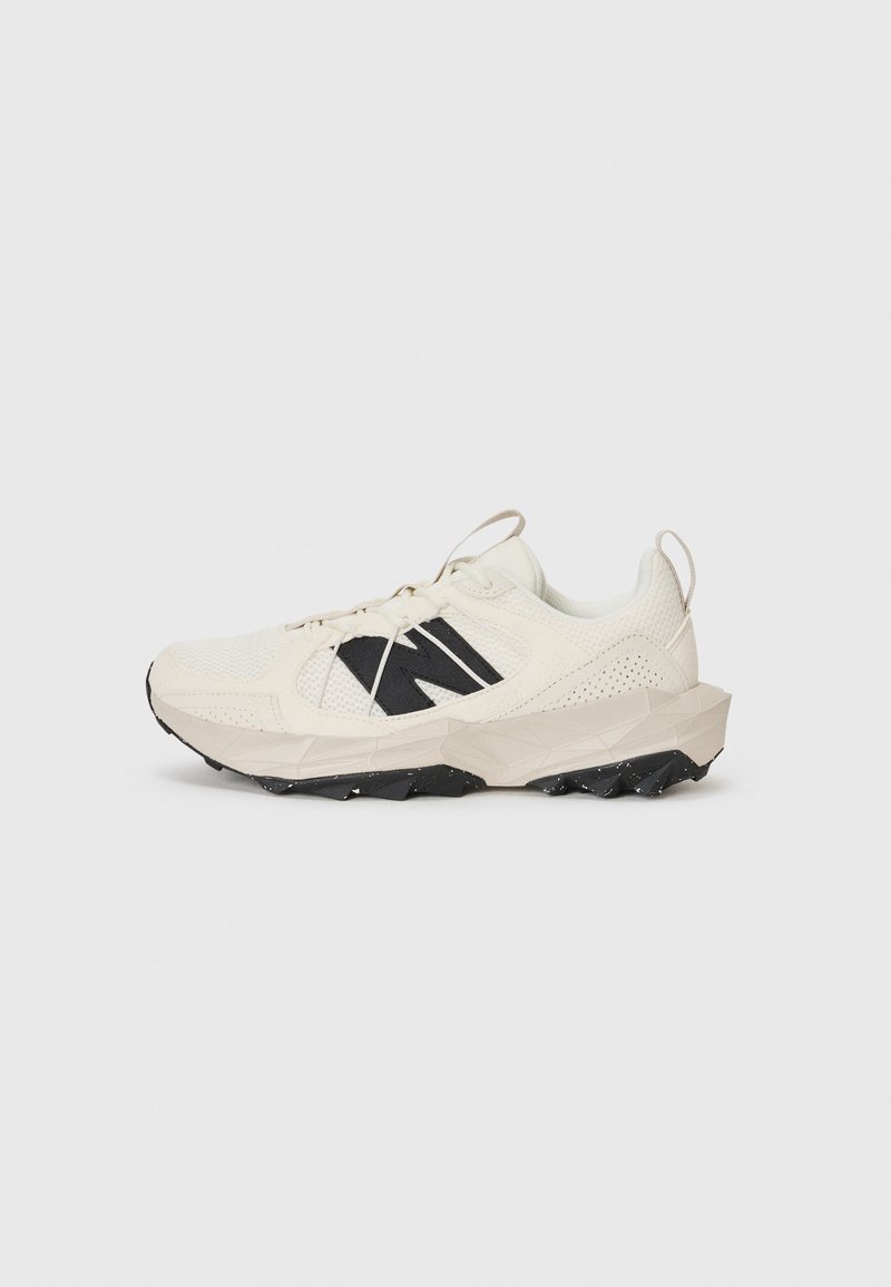 Light beige sneaker featuring a mesh upper, black logo, and textured sole. Accented with a geometric pattern on the midsole.