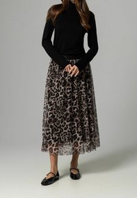 Sort turtleneck sweater parret med en gennemsigtig maxi-nederdel i leopardprint i nuancer af brun og beige, suppleret med sorte flade sko.