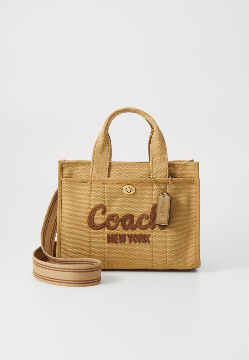 Bézs színű kézitáska hímzett "Coach New York" logóval. Két füllel, levehető pánttal és cipzáras záródással rendelkezik.