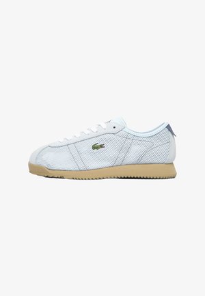 Zapatilla baja de malla blanca con suela beige, cordones blancos y logo verde de cocodrilo en el lateral.