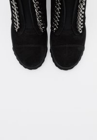 Czarne zamszowe botki za kostkę o dopasowanym kroju, z dekoracyjnym srebrnym łańcuchem wzdłuż boków oraz teksturowanymi gumowymi podeszwami.