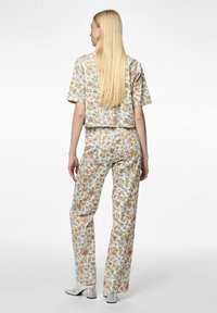 Top corto con estampado floral y pantalones de pierna ancha a juego en tela ligera. Los colores incluyen amarillo, rosa, azul y verde con un acabado texturizado.