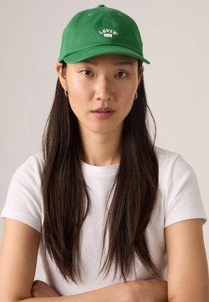 Green cotton baseball cap featuring white "Levi's" logo, with a curved visor and ventilation eyelets. Worn with a white t-shirt.