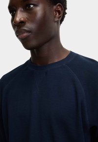 Maglione lavorato a maglia blu navy con texture a coste, scollo rotondo e maniche raglan. Presenta dettagli di cucitura sottili lungo le cuciture.