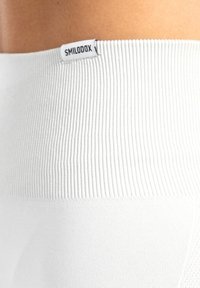 Witte geribbelde tailleband met een gladde textuur en contrasterend logo-label. Ontworpen voor een strakke pasvorm, die functionaliteit en comfort combineert.