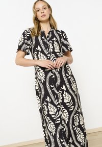 Abito maxi nero con motivo floreale, maniche corte e chiusura a bottoni. Presenta disegni bianchi a forma di foglia e una vestibilità comoda. Tessuto dalla consistenza liscia.