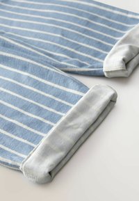 Tissu rayé bleu et blanc avec des poignets roulés gris clair sur une surface plane.