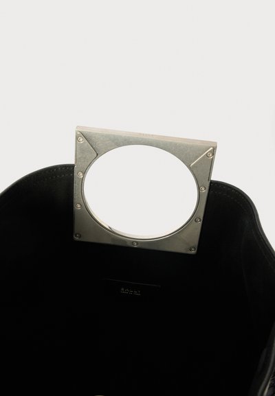 Black leather tote bag with a silver metal handle featuring a circular cutout. Smooth texture with a simple design and no visible patterns.