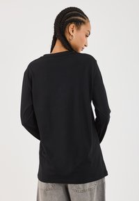 Schwarzes Langarmshirt aus weicher Baumwolle. Es hat einen runden Halsausschnitt und eine entspannte Passform, mit gepufften Ärmeln und einem schlichten Rückendesign.
