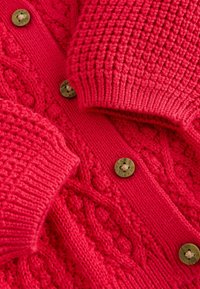 Rdeč pleteni kardigan z teksturiranimi vzorci v obliki kit, rebrastimi manšetami in kontrastnimi gumbi z vgraviranimi detajli. Mehka in gosta tkanina.