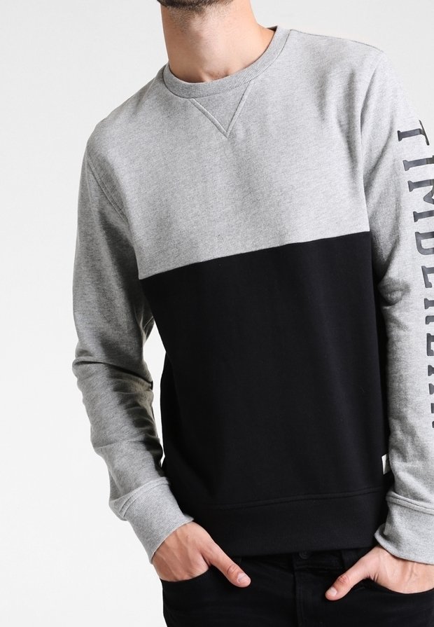 Grijs-zwarte crewneck-trui met horizontaal kleurvlakkenontwerp, geribbelde manchetten en tekstdetail langs één mouw.