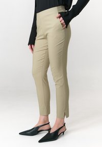 Beige, maßgeschneiderte Hose mit seitlichen Taschen, konischer Form und seitlichen Schlitzen am Saum, kombiniert mit schwarzen Slingback-Pumps mit spitz zulaufender Zehenpartie.