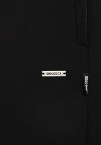 Black fabric with a ribbed texture, featuring a silver metal label that reads "SMILODOX" and a small black tag on the side.