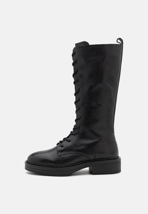 Czarne, sznurowane botki do kolan wykonane z gładkiej skóry. Posiadają okrągły czubek oraz płaską, teksturowaną podeszwę, z uchwytem z tyłu.