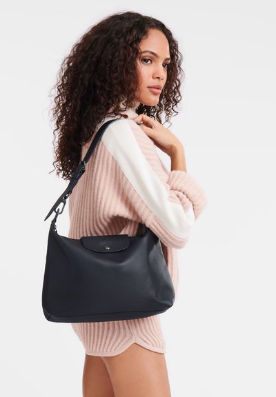 Schwarze Leder-Schultertasche mit Klappe und Druckverschluss, präsentiert sich in glatter Textur und minimalistisches Design. Verstellbarer Tragegurt inklusive.