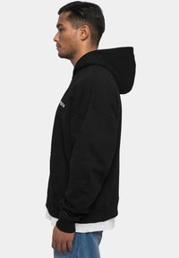 Sweatshirt à capuche noir avec une coupe décontractée, doté d'une poche kangourou, de poignets côtelés et d'un subtil détail de logo sur la poitrine.
