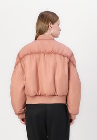 Padded bomber jacket in soft peach, featuring a ribbed collar and cuffs, with a loose fit and elasticized hem. Smooth, glossy texture.