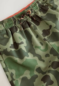 Shorts de bain en camouflage vert avec une taille élastique, un cordon de serrage ajustable et une texture de tissu lisse et léger.