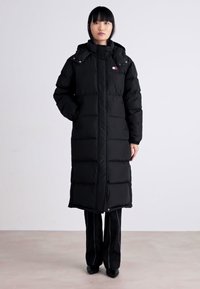 Cappotto lungo nero imbottito realizzato in materiale isolante, con colletto alto, chiusura a zip e sezioni trapuntate ben visibili.