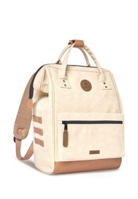 Mochila beige con tela crema, detalles en cuero marrón, asas superiores, un bolsillo frontal con cremallera y detalles de cintas laterales.