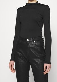 Maglietta nera a maniche lunghe con collo alto; abbinata a jeans neri lucidi con un classico design a cinque tasche e dettagli metallici.