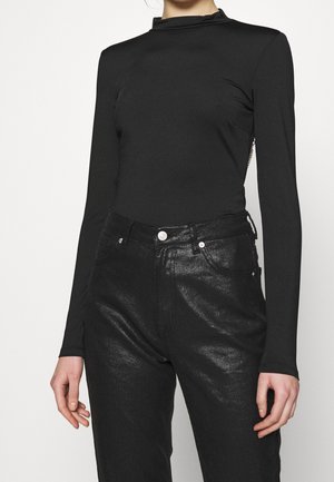 Schwarzes Langarmoberteil mit Stehkragen; kombiniert mit glänzenden schwarzen Jeans im klassischen Fünf-Taschen-Design und metallischen Akzenten.