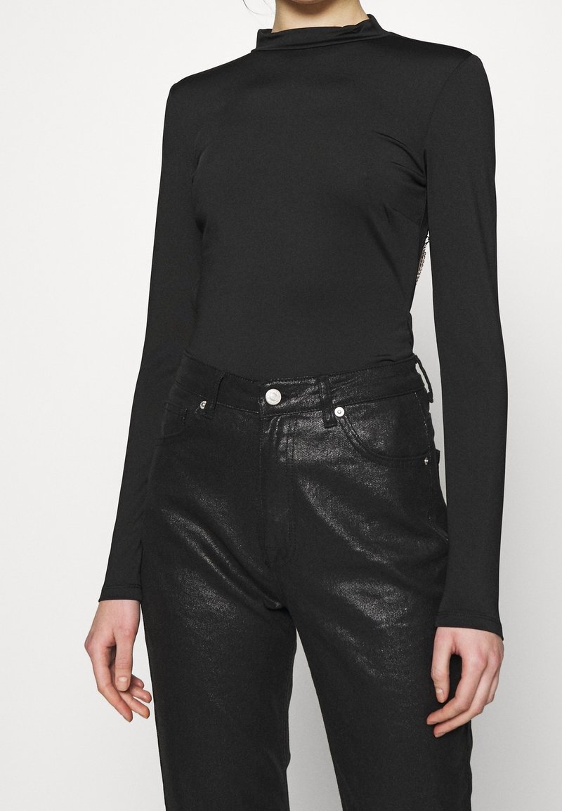 Maglietta nera a maniche lunghe con collo alto; abbinata a jeans neri lucidi con un classico design a cinque tasche e dettagli metallici.
