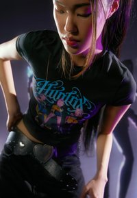 Czarny t-shirt z kolorowym nadrukiem graficznym; czarny pasek z wysokim stanem, ozdobiony klamrą w kształcie serca i ćwiekami; luźny fason.