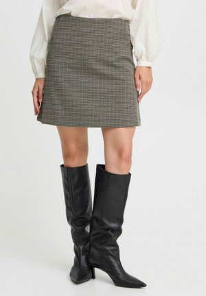 Houndstooth mini skirt in beige and black, featuring a fitted design. Paired with knee-high black leather boots with a pointed toe.