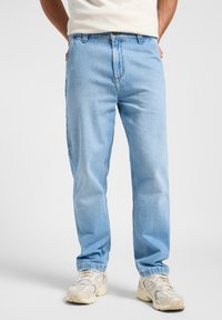 Jeans de mezclilla azul claro con un corte relajado, que presentan un diseño de cinco bolsillos y cierre de botón. Se llevan con zapatillas blancas y una camiseta básica.