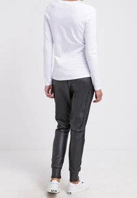 Bílá dlouhá halenka spárovaná s úzkými černými veganskými koženými kalhotami a bílými teniskami, které ukazují štíhlou siluetu a minimalistic design.