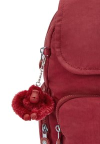 Zaino in stoffa rosso con superficie testurizzata, dotato di un portachiavi in peluche a forma di gorilla rimovibile e compartimenti con zip con accessori in metallo argentato.
