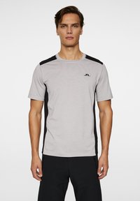 Grå sportströja med svarta sidopaneler och korta ärmar. Har en rund halsringning och en liten logotyp på bröstet.