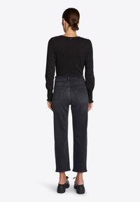 Camicia nera a maniche lunghe con dettaglio elastico ai polsini, abbinata a jeans grigi scuri a vita alta e ghette nere.