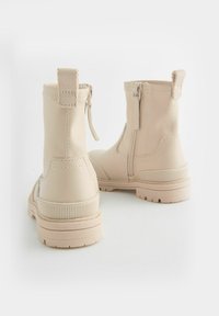 Bottines beiges en matériau synthétique avec des fermetures éclair sur les côtés, des semelles en caoutchouc texturé et des languettes à l'arrière. Design minimaliste.