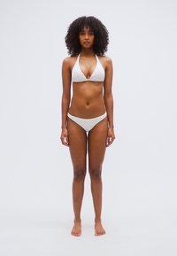 Σετ λευκού μπικίνι με τοπ halter λαιμόκοψης και σλιπ χαμηλής μέσης, με λεία υφή, ελάχιστες ραφές και χωρίς σχέδια, παρουσιάζεται σε μοντέλο.