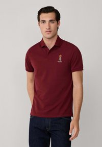 Burgundská polo košela zo zmesi bavlny s krátkymi rukávmi, s vyšitým logom na ľavej hrudi a klasickým golierom.
