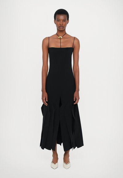 Μαύρο αμάνικο φόρεμα με εφαρμοστό κορσάζ και ασύμμετρο, στρωτό το κάτω μέρος. Λείο ύφασμα; περιλαμβάνει μια διακριτική σχισμή και ελάχιστη μεταλλική λεπτομέρεια.